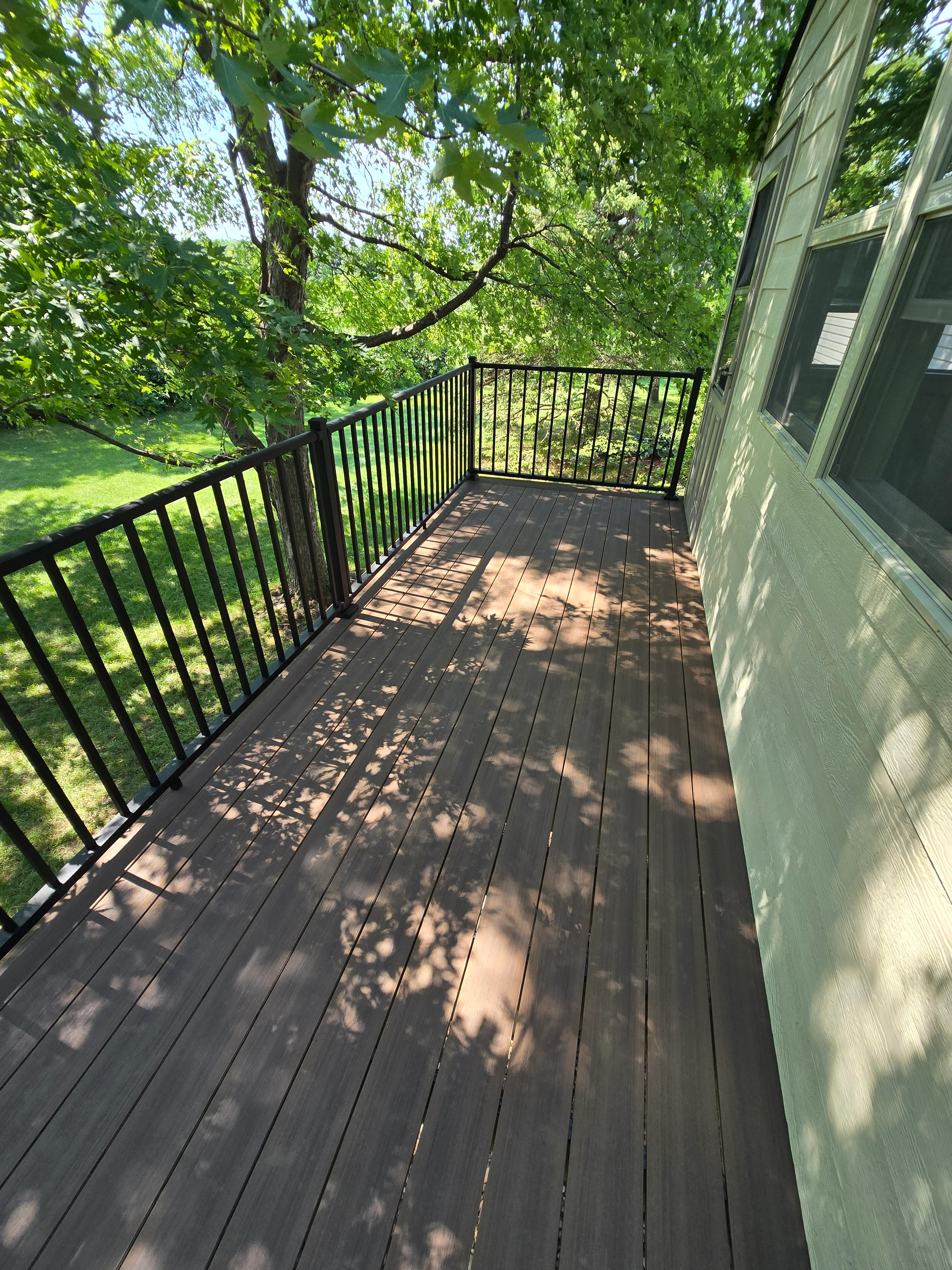 Dark composite deck with black aluminum railing overlooking wooded yard