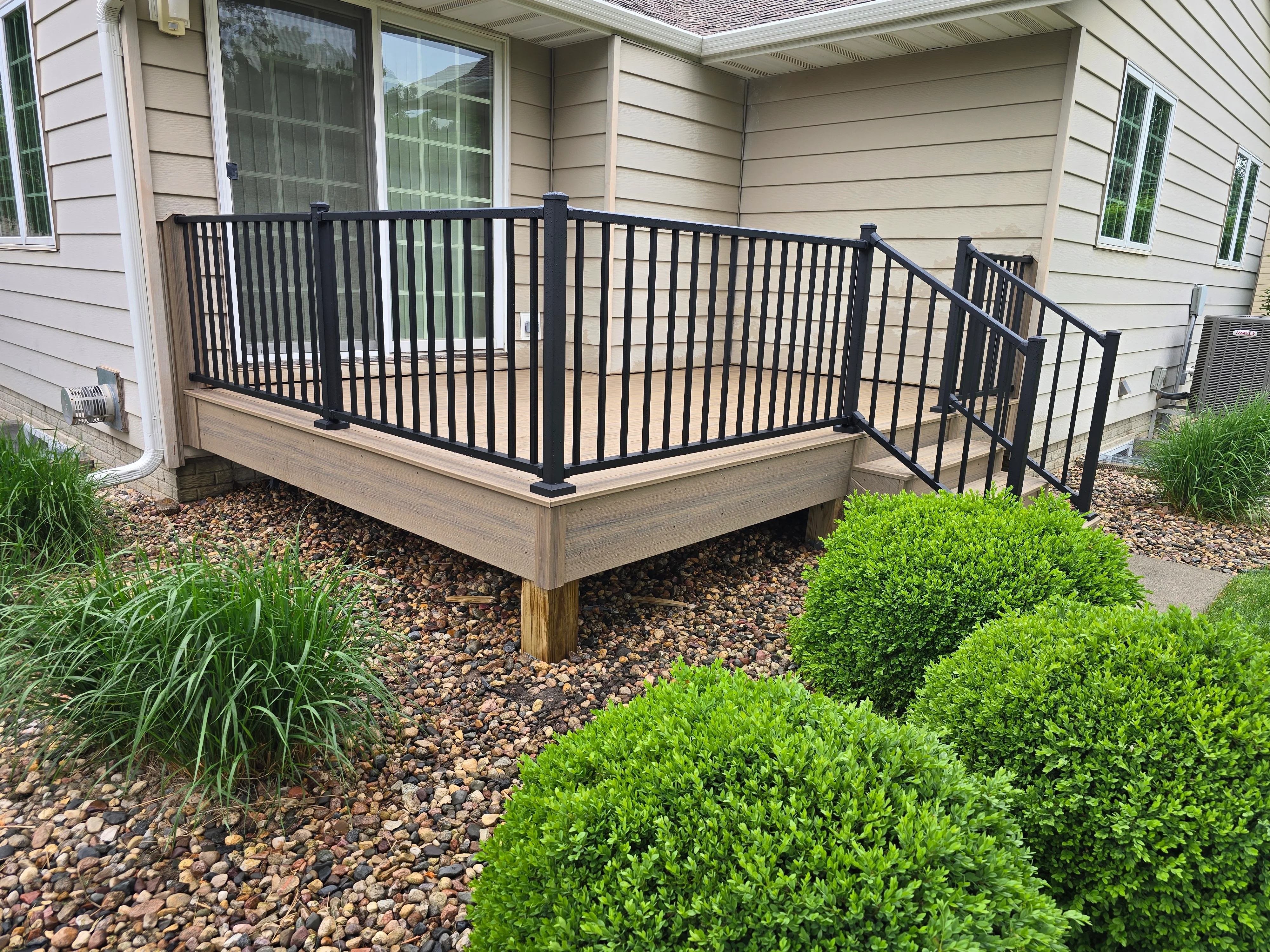 Elevated composite deck with black aluminum railings and stairs, surrounded by landscaping