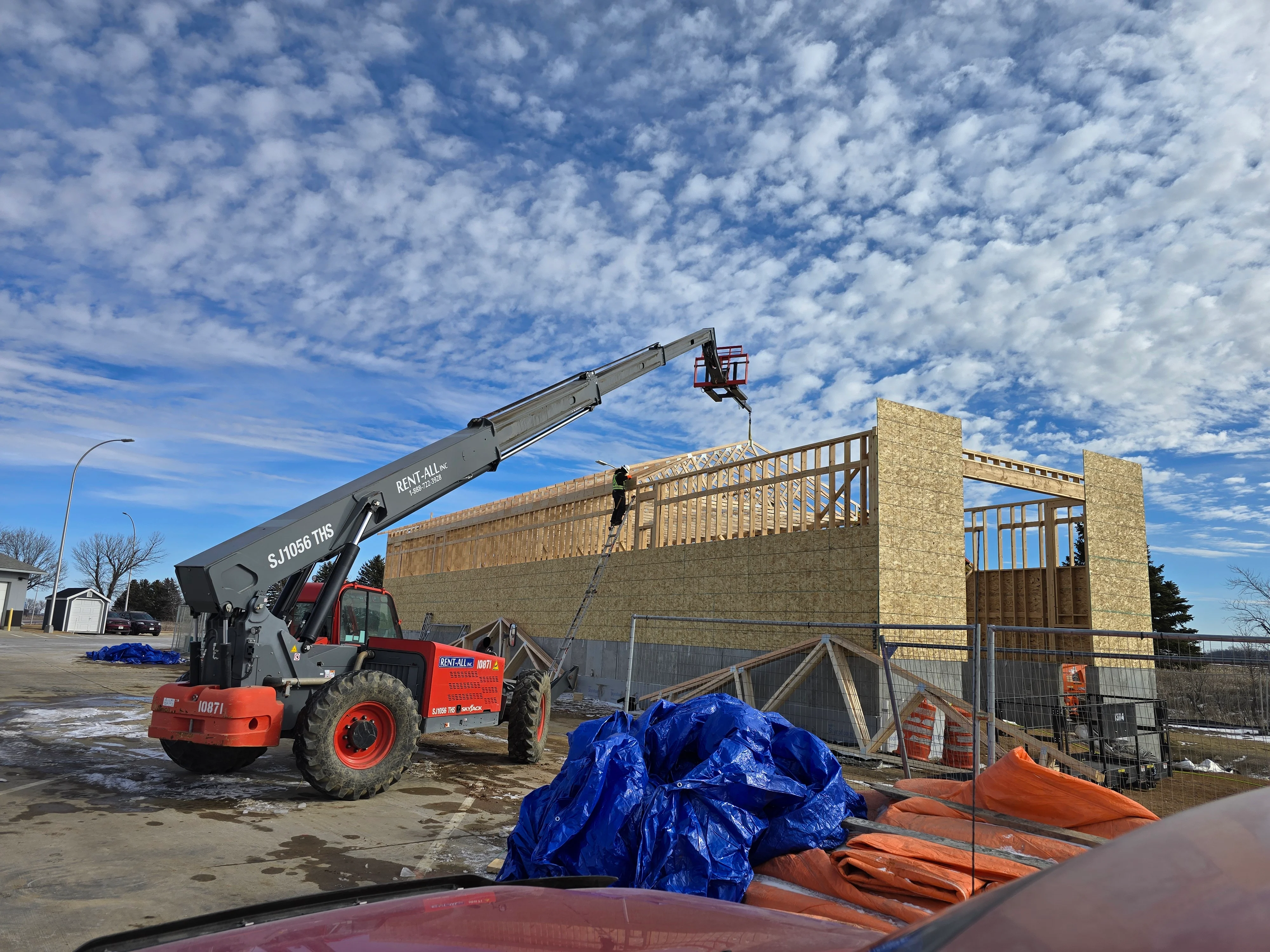 Telescopic handler lifting framing materials at commercial construction site with masonry walls