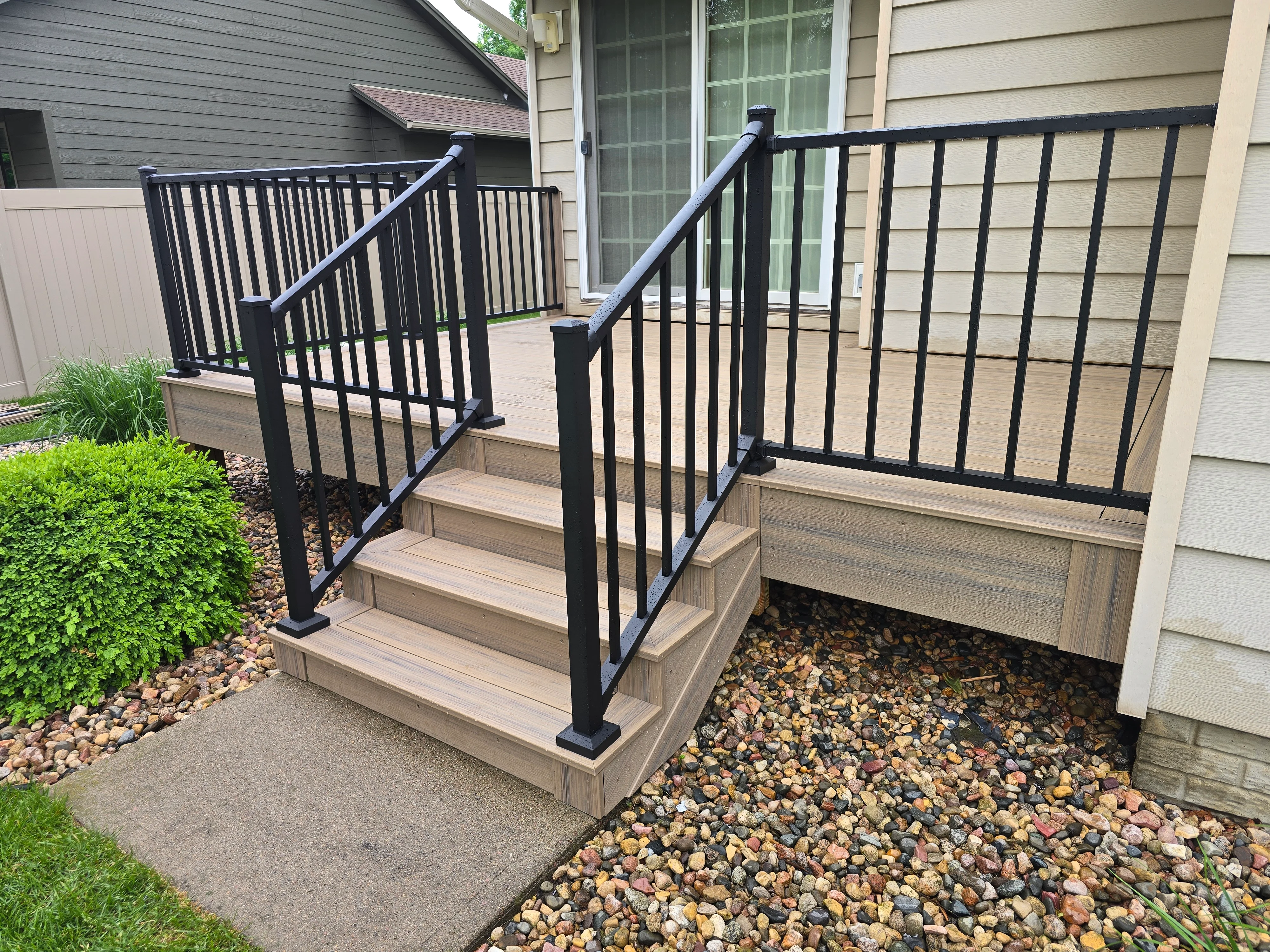 Composite deck stairs with black metal railing and handrail on residential home